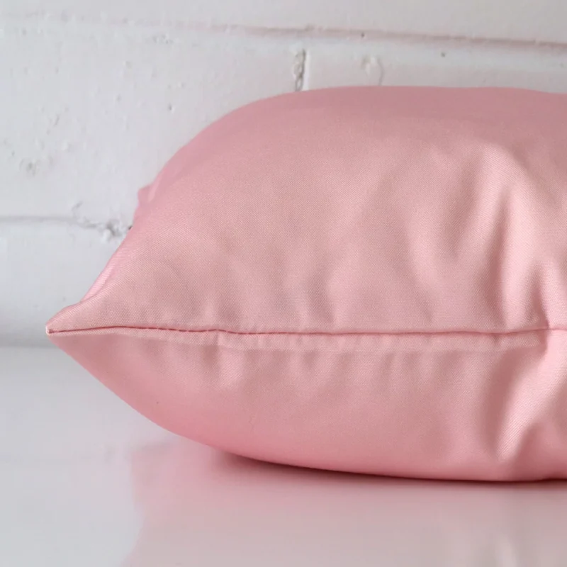 Square outdoor cushion cover positioned flat to show seams. The pink hue is shown between front and rear fabric panels.