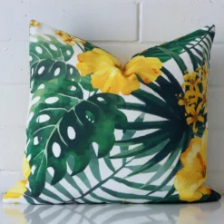 White wall with a tropical yellow cushion laying against it. It has a distinctive outdoor fabric and has a square shape.