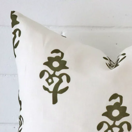 Corner section image showing features of square olive green cushion that has a patterned motif on its linen fabric.