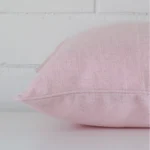 Square pink cushion laid flat. This view shows the linen fabric from side on.