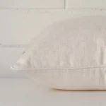 Cream cushion cover laying sideways against brick wall. The square size and linen material are shown highlighting the seams.