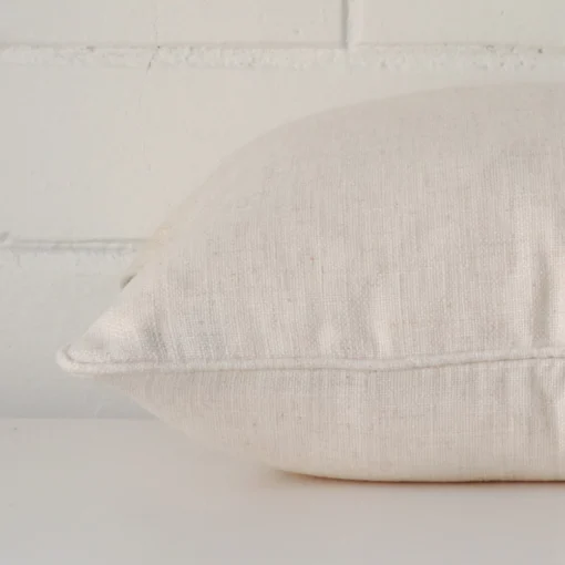 Cream cushion cover laying sideways against brick wall. The square size and linen material are shown highlighting the seams.