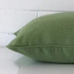The edge of this linen square cushion in sage green is shown.