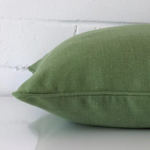 The edge of this linen square cushion in sage green is shown.