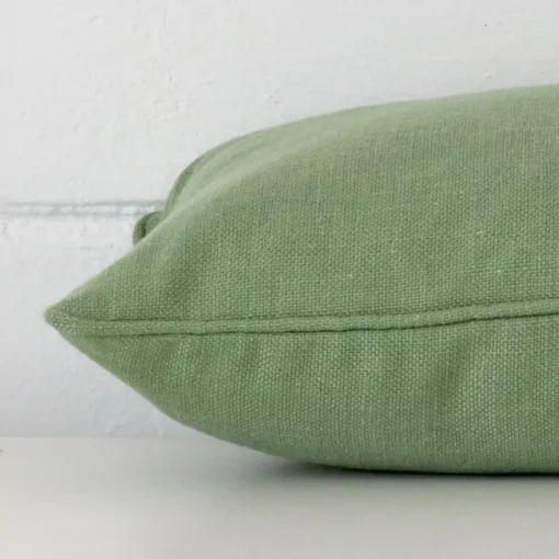 Sage green cushion cover laying sideways against brick wall. The rectangle size and linen material are shown highlighting the seams.