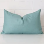 Bold rectangle teal cushion positioned in front of white brickwork. It is made from linen fabric.
