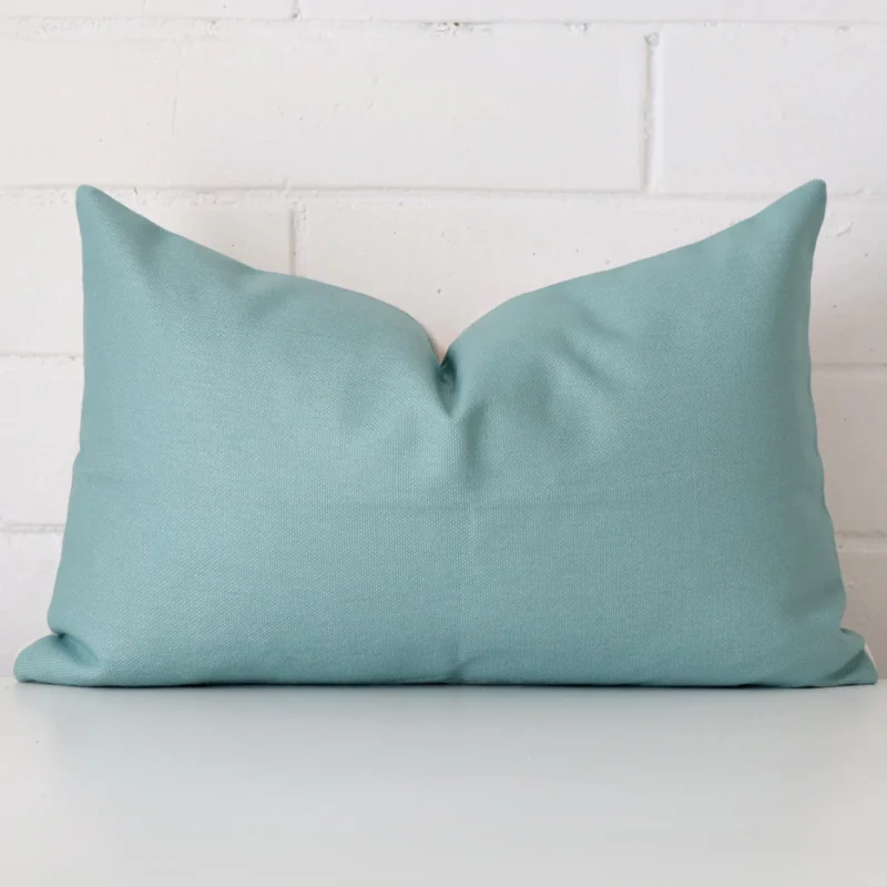 alfama-teal-rectangular-cushion-cover-30cm-x-50cm-sc374-30 Bold rectangle teal cushion positioned in front of white brickwork. It is made from linen fabric.