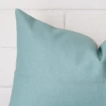 Rectangle cushion in teal colour sitting upright in front of a brick wall. It has been made from a quality linen material.