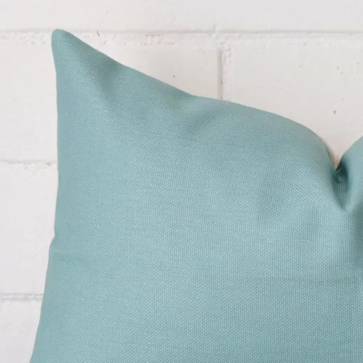 Rectangle cushion in teal colour sitting upright in front of a brick wall. It has been made from a quality linen material.