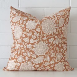 Bold square terracotta cushion positioned in front of white brickwork. Its floral style pops on the linen fabric.