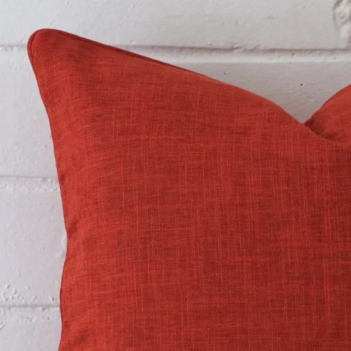 The corner of this burnt orange linen cushion is shown close up. It has a square design.