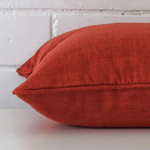 Close side shot of this burnt orange cushion cover. It has a square design.