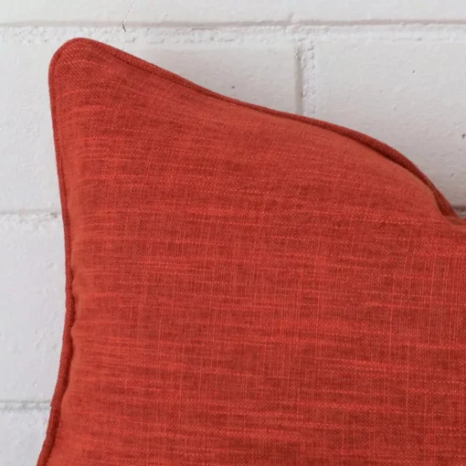 Close up view showing a corner of this linen cushion in a rectangle size and with burnt orange colouring.