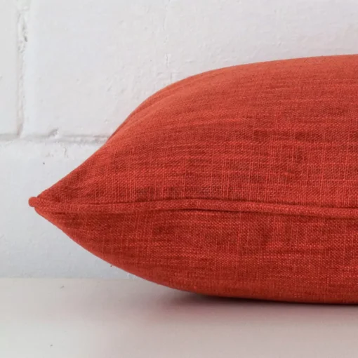 Burnt orange cushion laid horizontally. This perspective shows the edge of the linen fabric and its rectangle shape.