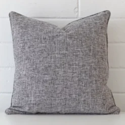 Bold square grey cushion positioned in front of white brickwork. It is made from a linen fabric.
