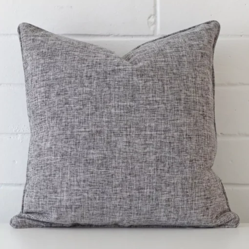 Bold square grey cushion positioned in front of white brickwork. It is made from a linen fabric.