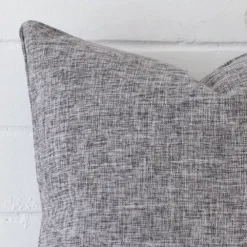 Square cushion in grey colour sitting upright in front of a brick wall. It has been made from a quality linen material.