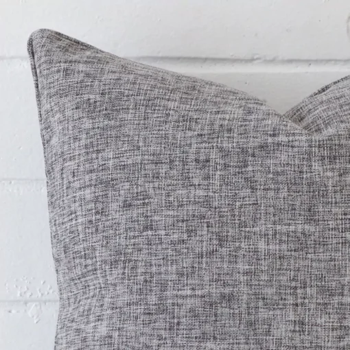 Square cushion in grey colour sitting upright in front of a brick wall. It has been made from a quality linen material.