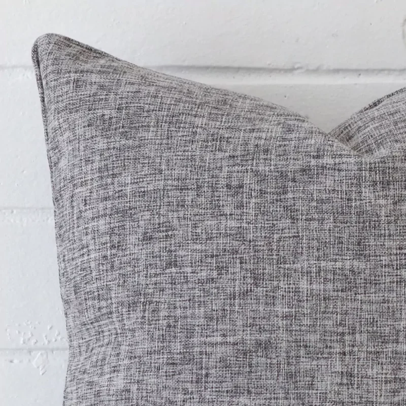 Square cushion in grey colour sitting upright in front of a brick wall. It has been made from a quality linen material.