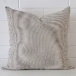 White wall with a striped style cushion laying against it. It has a distinctive designer fabric and has a square shape.