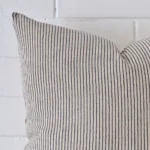 Square striped cushion sitting upright in front of a brick wall. It has been made from a quality designer material.