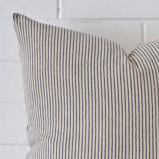 Square striped cushion sitting upright in front of a brick wall. It has been made from a quality designer material.