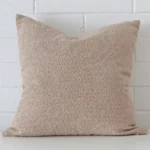 White wall with a beige cushion laying against it. It has a distinctive boucle fabric and has a square shape.