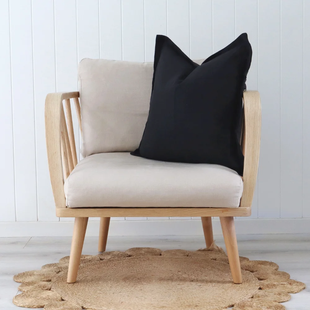 A black cushion sits at a slight angle on a light coloured armchair.
