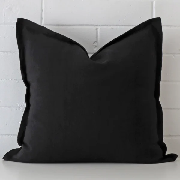 Linen square cushion in an upright position against a white brick wall. It is black in colour.