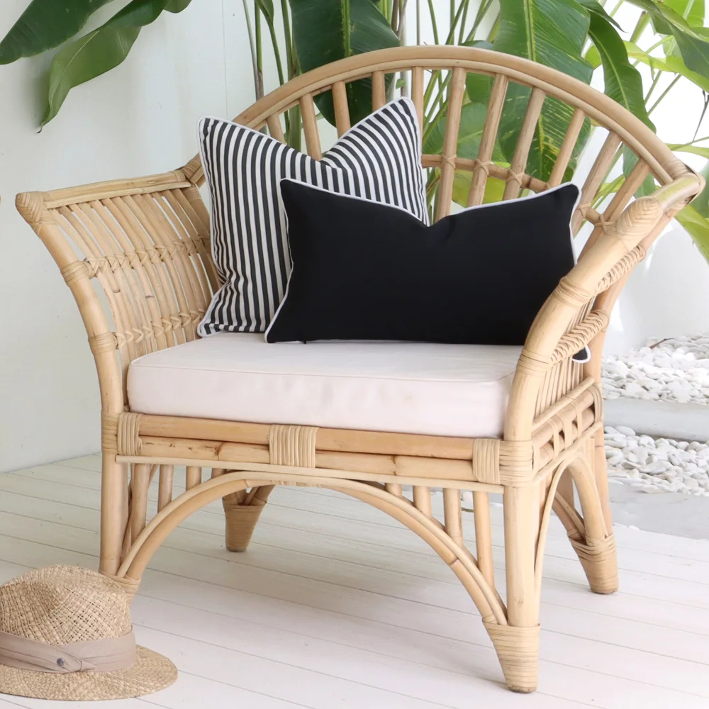 Two black outdoor cushions styled on a rattan chair.