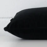 Rectangle black cushion laid flat. This view shows the velvet fabric from side on.