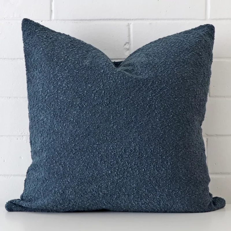 blue-boucle-cushion-cover-large-sc1032-55 Square cushion cover in blue colour sitting upright in front of a brick wall. It has been made from a quality boucle material.