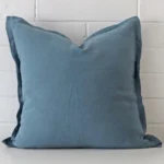 Blue linen cushion cover features prominently against a white wall. It is a square design.