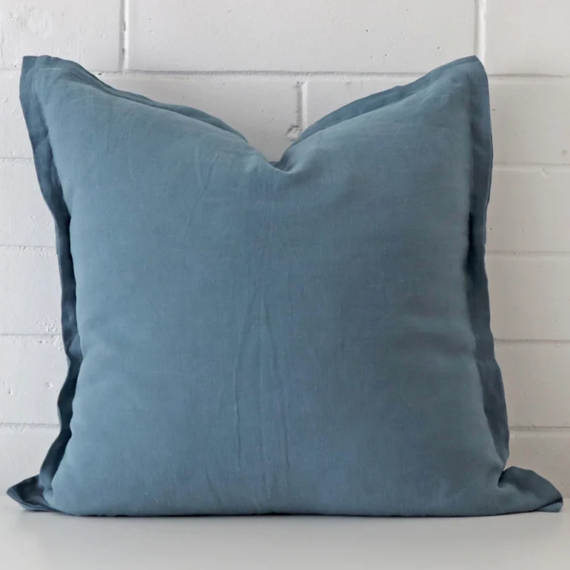 blue-linen-cushion-cover-sc813-55 Blue linen cushion cover features prominently against a white wall. It is a square design.