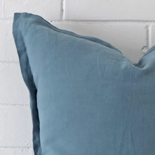 Focused view of square cushion cover. The shot shows details of its linen material and blue colour.