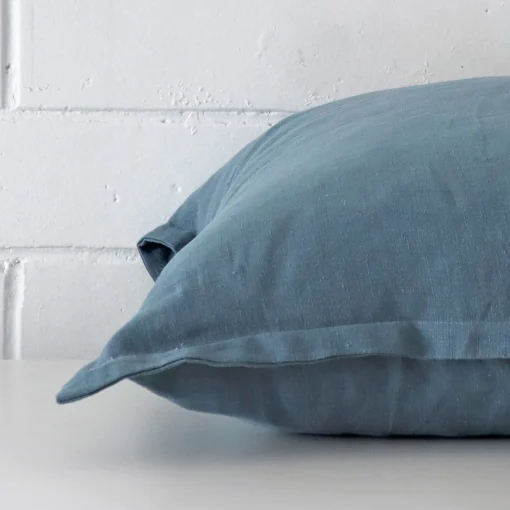 Blue linen cushion cover laying sideways against brick wall. The square size and linen material are shown highlighting the seams.