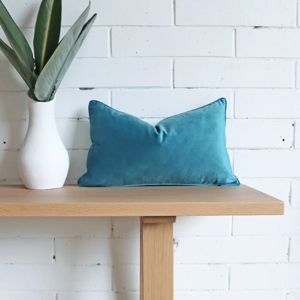 A blue velvet cushion placed on a bench seat with a plant nearby.