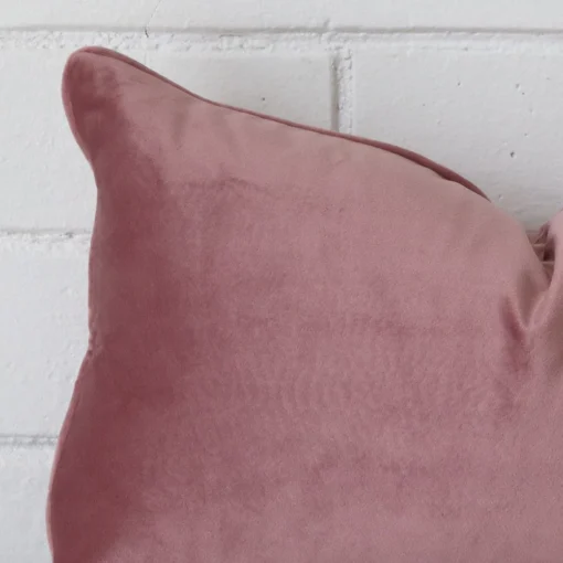Close up view showing a corner of this velvet cushion in a rectangle size and with blush colouring.
