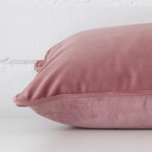 Blush cushion cover laying sideways against brick wall. The rectangle size and velvet material are shown highlighting the seams.