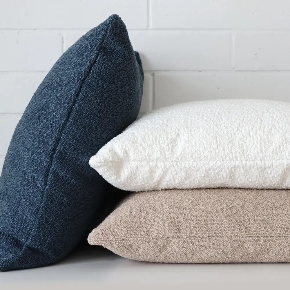 Three boucle cushions have been stacked against a white wall.