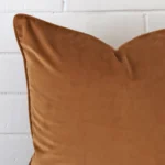 Square cushion in bronze colour sitting upright in front of a brick wall. It has been made from a quality velvet material.