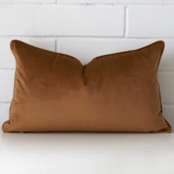 Bronze velvet cushion cover in front of a white wall. It has a large size and is made from a velvet material.
