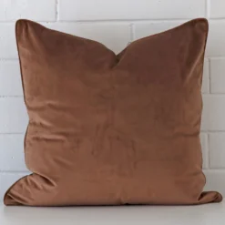 Square cushion cover in brown colour sitting upright in front of a brick wall. It has been made from a quality velvet material.