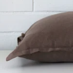 Chocolate brown cushion cover laying sideways against brick wall. The square size and linen material are shown highlighting the seams.