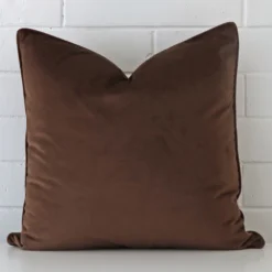 Chocolate brown velvet cushion cover features prominently against a white wall. It is a square design.