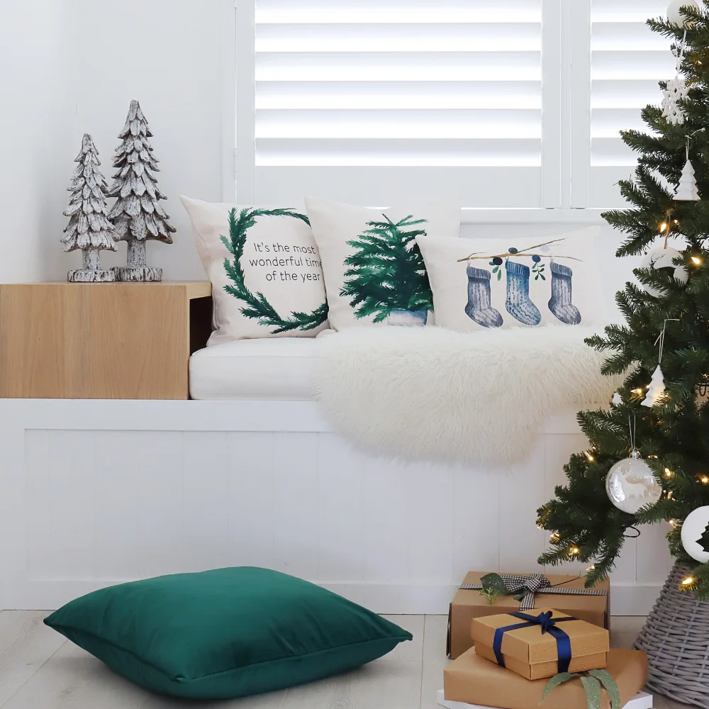 Three Christmas cushions have been styled on a window seat near a tree.