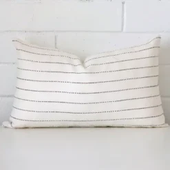 An attractive striped linen cushion in front of a white brick wall. It has a rectangle shape.