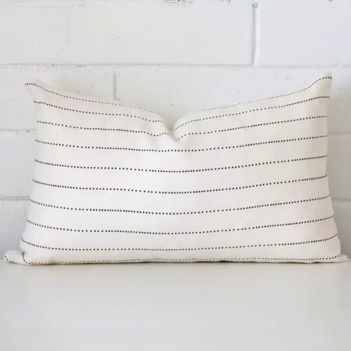 An attractive striped linen cushion in front of a white brick wall. It has a rectangle shape.