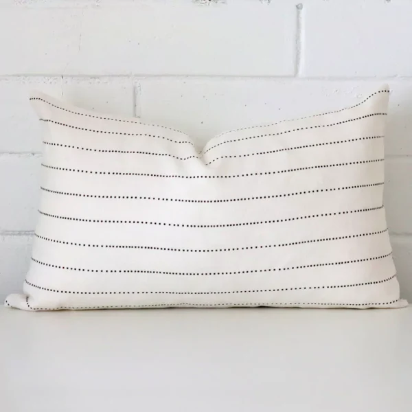 An attractive striped linen cushion in front of a white brick wall. It has a rectangle shape.