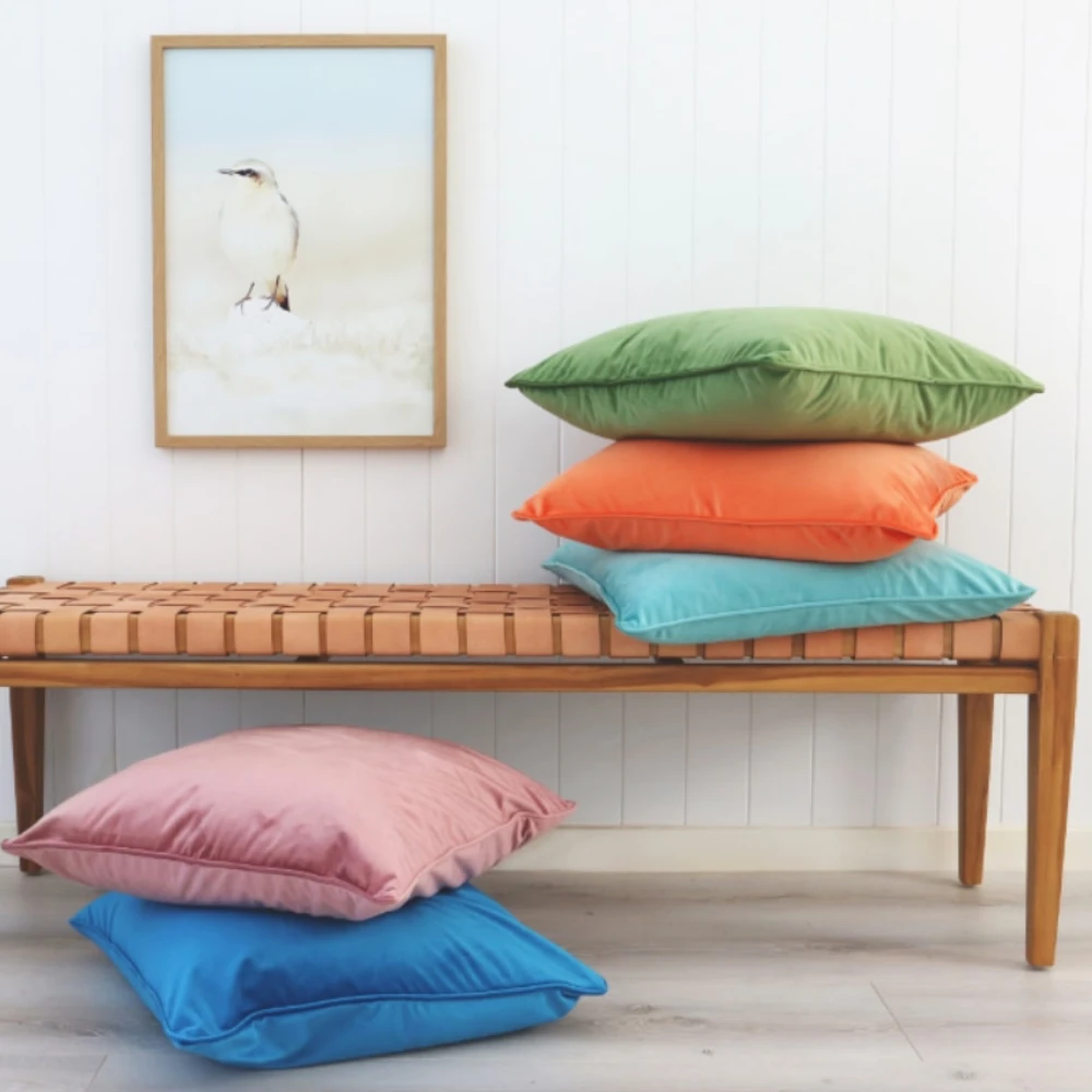 Colourful cushions in two stacks sit near a wood and leather bench.